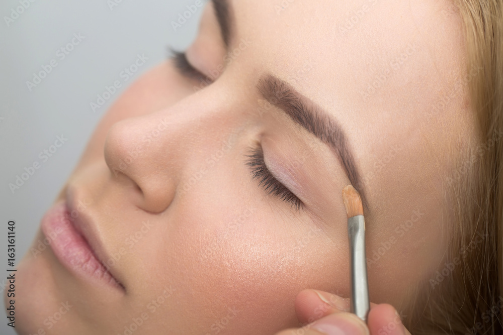 Girl with closed eyes getting makeup on eyelids