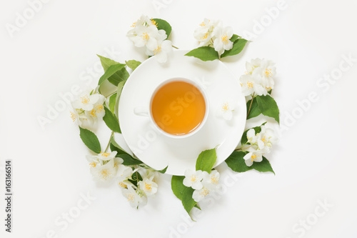 Jasmine flowers around cup of green tea on white background. Top view and concept.