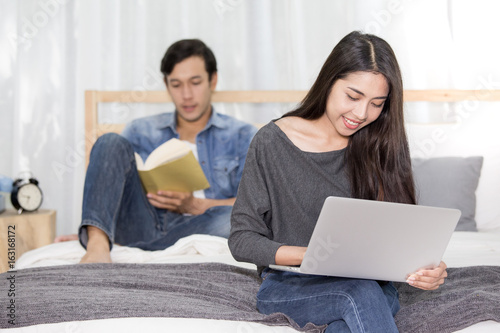 Young woman using laptop and man reading book on bed, people lifestyle concept.