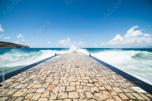 Rough sea waves against the pier with blue sky and clouds photo