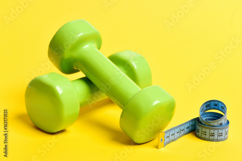 Twisted measuring tape in blue color and green dumbbells