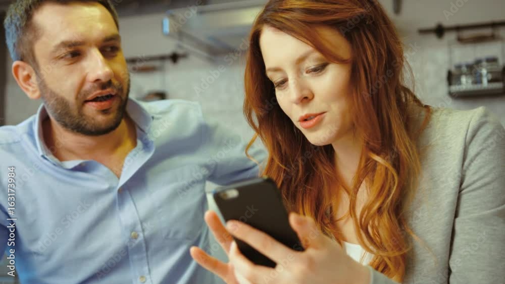 Happy young couple watching smart phone together sitting on a sofa in a living room at modern loft interior. Indoor. Happy young couple watching smart phone together sitting on a sofa in a living room at modern loft interior. Indoor.