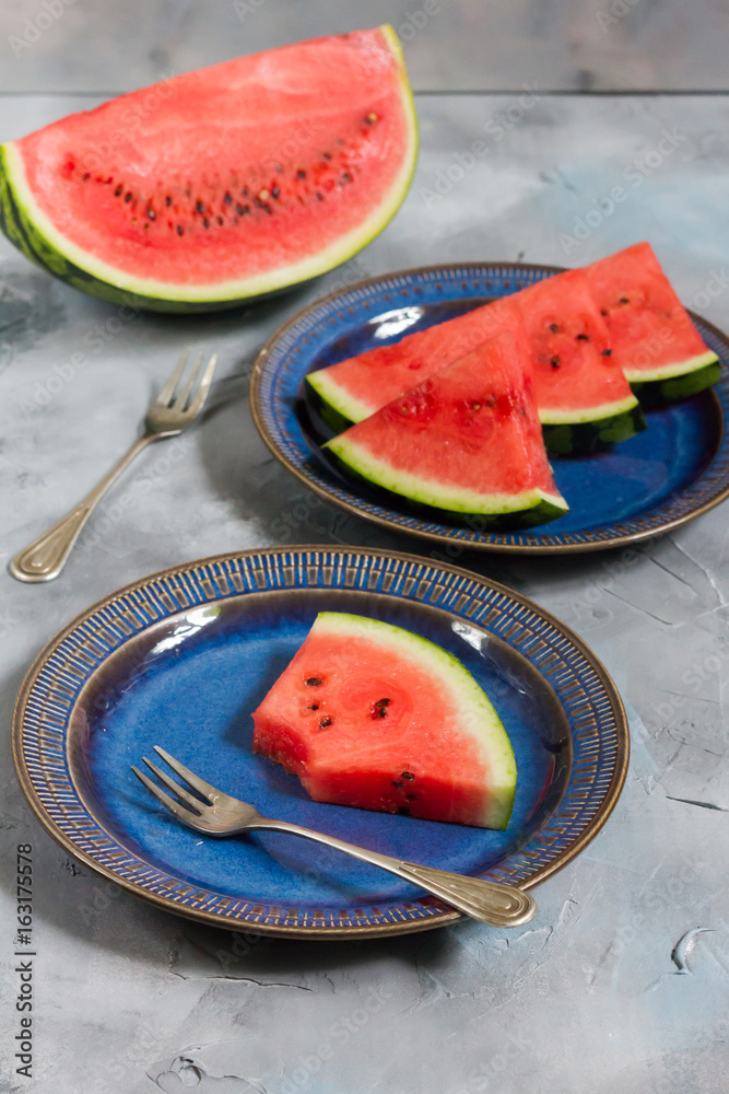 Pieces of watermelon on a dark blue plate. Grey background. Pieces of watermelon on a dark blue plate. Grey background.