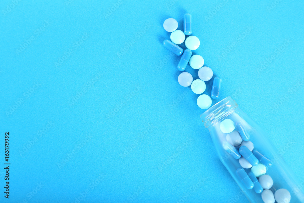 Blue pills in glass bottle on blue background Blue pills in glass bottle on blue background