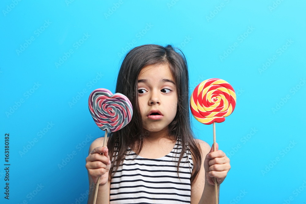 Beautiful little girl with lollipop on blue background
