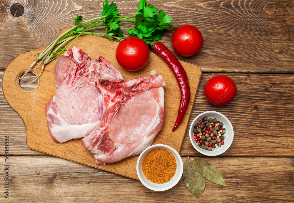 A piece of raw meat, pork with vegetables and spices on a dark, wooden background. Banner for the restaurant. A piece of raw meat, pork with vegetables and spices on a dark, wooden background. Banner for the restaurant.
