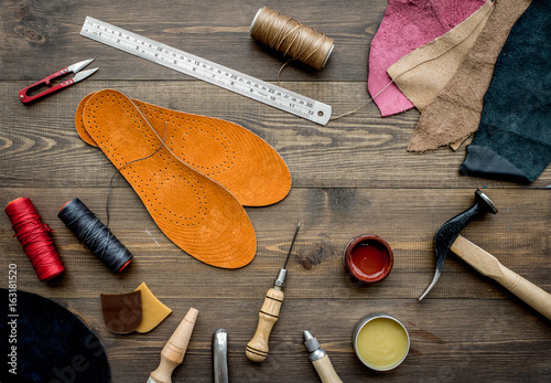 Set of cobbler tools on brown wooden desk background top view