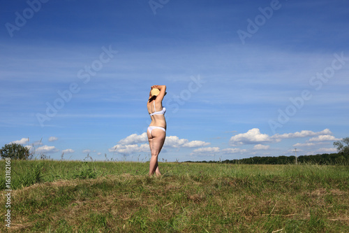 Kobieta w bieliźnie z boku na tle nieba i łąki.