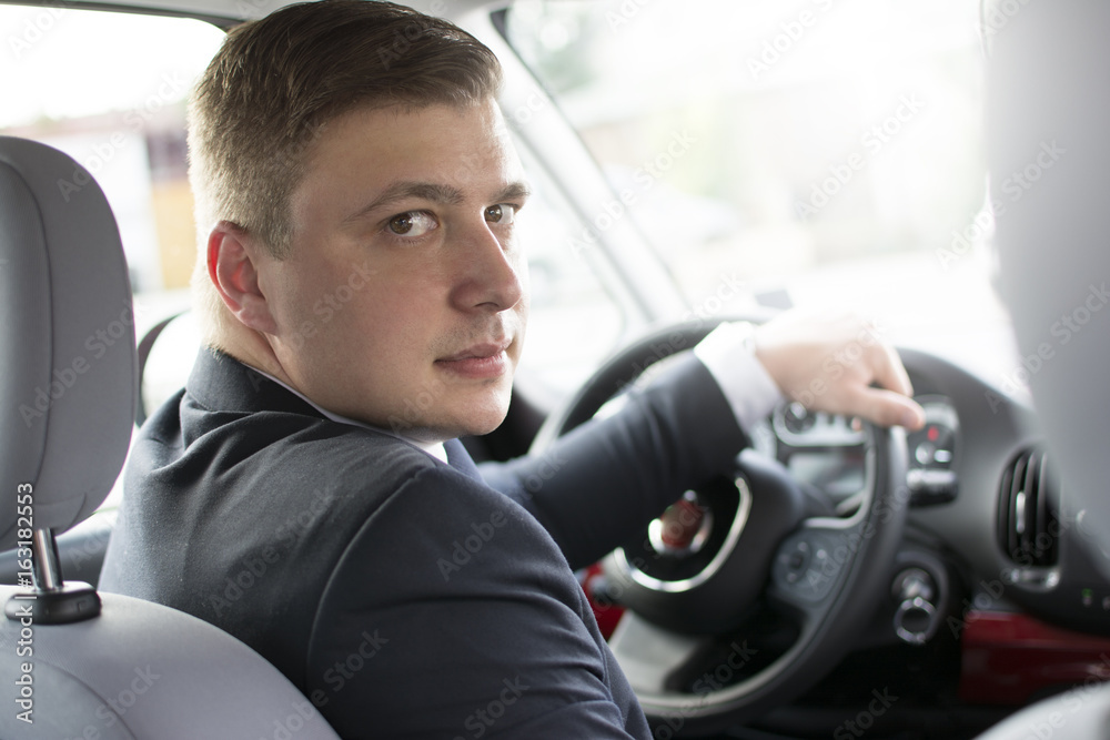 Modern businessman sitting in his car. Looking back at the camera. A successful businessman holding a steering wheel. Lens Flare in the background. Modern businessman sitting in his car. Looking back at the camera. A successful businessman holding a steering wheel. Lens Flare in the background.