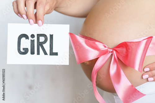 tummy with pink ribbon and bow of pregnant caucasian woman which is holding nameplate girl