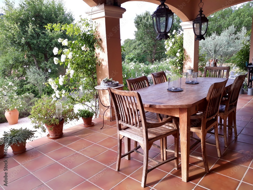 Cosy, french patio in provence with wooden garden furniture, surrounded by beautiful, white roses