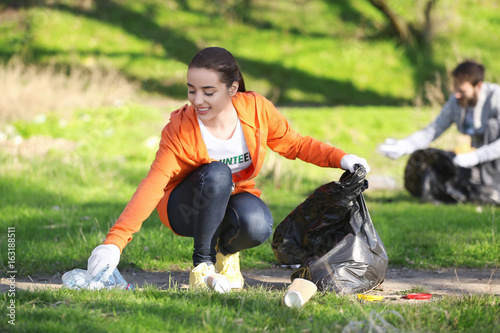 Young beautiful volunteer picking up litter in park