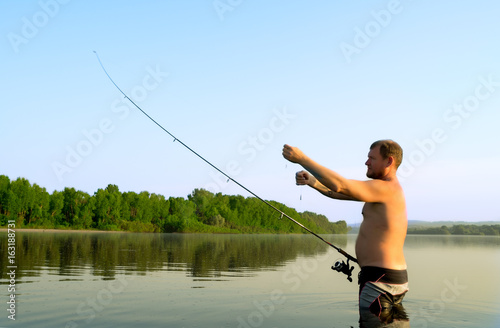 fisherman fishing in a calm river in the morning. Man in fishing gear stending in a river and throws a fishing pole