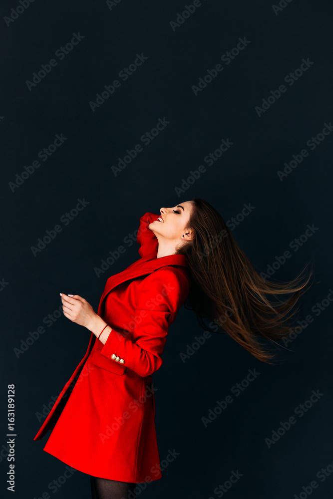 Young gorgeous model in red coat throwing her hair on dark background Young gorgeous model in red coat throwing her hair on dark background