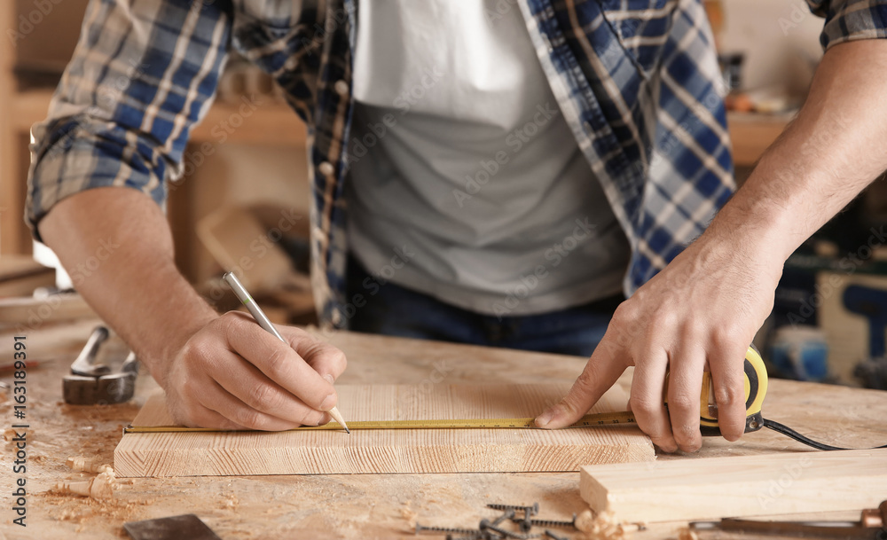 Carpenter marking measurements on piece of wooden board Carpenter marking measurements on piece of wooden board