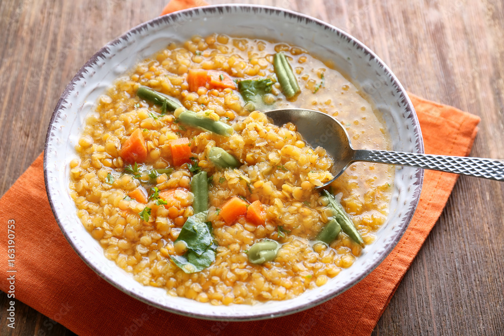 Eating tasty lentil dish with vegetables on wooden table, closeup