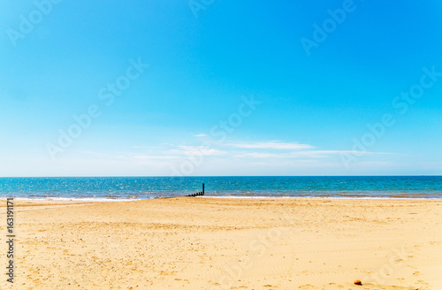Dock pilings on a sandy beach, blue ocean and yellow sand, sunny hot day in seaside resort