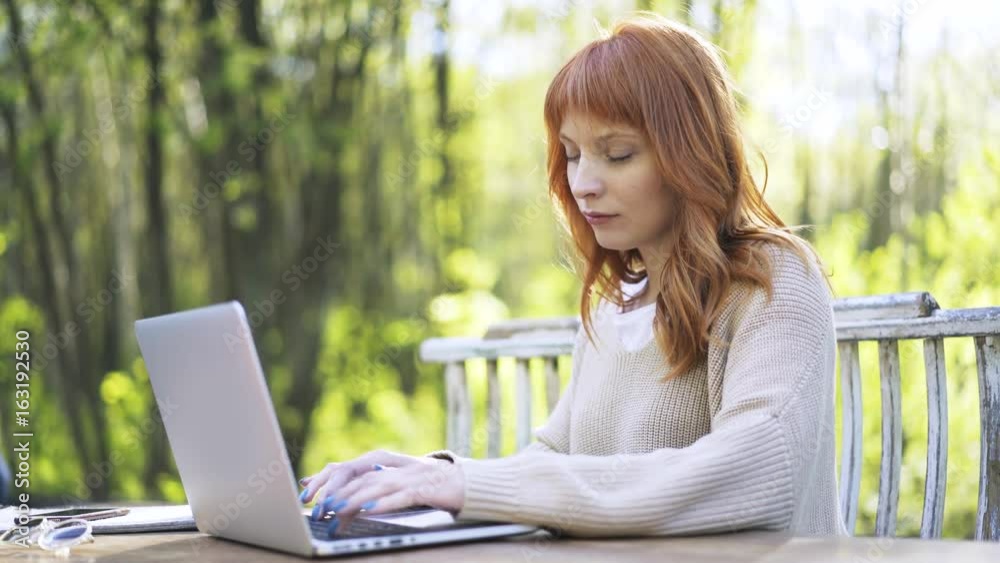 Side view of a beautiful redhead woman typing with her blue fingernail polish fingers sitting on a bench in a park. Locked down real time medium shot Side view of a beautiful redhead woman typing with her blue fingernail polish fingers sitting on a bench in a park. Locked down real time medium shot