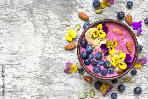 bowl of homemade smoothie topped with fresh blueberries, nuts, chia and pumpkin seeds and flowers