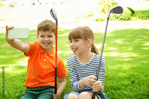 Cute children taking selfie while sitting on golf course in sunny day