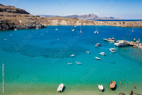 Ships on the Mediterranean blue lagoon. Greek rocky cliffs and the coast of the island of Rhodes. Beach and harbor. Leisure on the island of Rhodes.