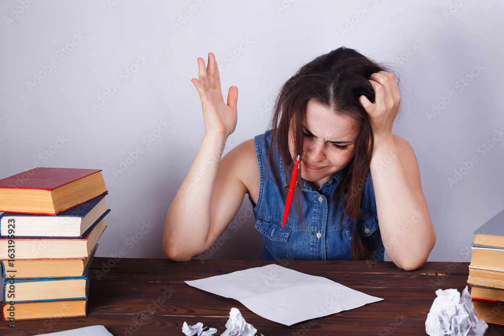 Young desperate pensive student woman sitting at the table with empty paper sheets, throwing a pen. Overwork, no inspiration, stress, routine concept Young desperate pensive student woman sitting at the table with empty paper sheets, throwing a pen. Overwork, no inspiration, stress, routine concept
