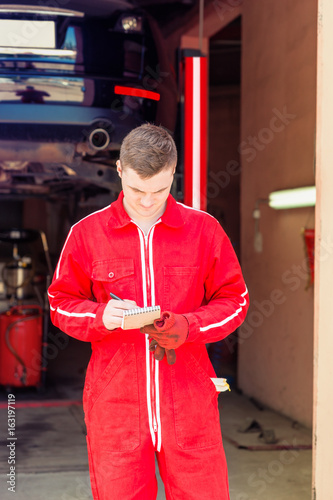 Male auto mechanic standing making notes
