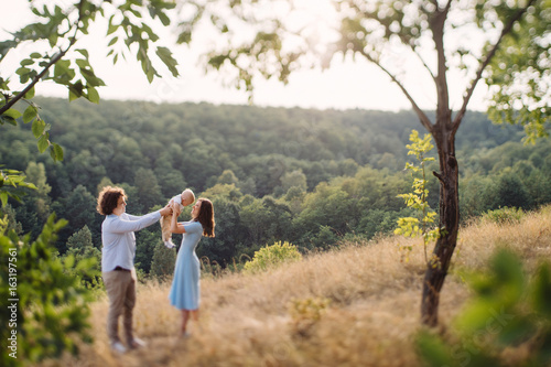 Young happy caucasian couple with little baby boy. Parents and son walking and having fun together. Mother and father playing with toddler outdoors. Family, parenthood, childhood, happiness concept.