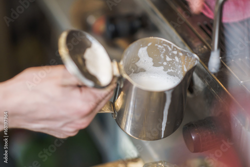 Young man bartender frothing milk foam on a barista machine