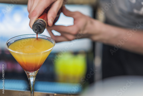 Young bartender making a colorful cocktail, pouring alcohol in a cocktail glass photo