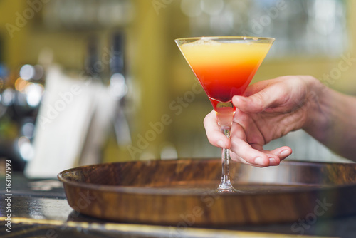 Young bartender making a colorful cocktail, pouring alcohol in a cocktail glass photo