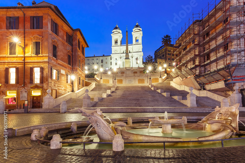 Monumental stairway Spanish Steps, seen from Piazza di Spagna, and the Early Baroque fountain called Fontana della Barcaccia or Fountain of the ugly Boat during morning blue hour, Rome, Italy.