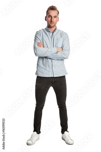 Good looking blonde man wearing a light blue shirt standing against a white background looking at camera.