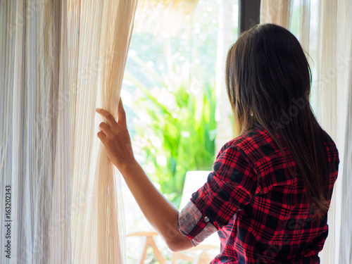 Rear view of a young woman holding the curtains open to look out of a large light window at home, interior. Positive and aspirational lifestyle. Sad Woman looking out a window, indoors. Free Download Rear view of a young woman holding the curtains open to look out of a large light window at home, interior. Positive and aspirational lifestyle. Sad Woman looking out a window, indoors. - GFXLoad