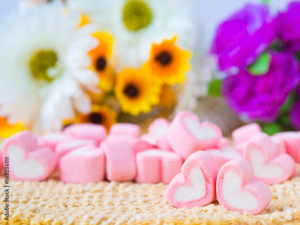 Closeup of sweet marshmallow in the shape of heart on wooden plate and flower at background. Concept about love and relationship. (Soft Style for Background)