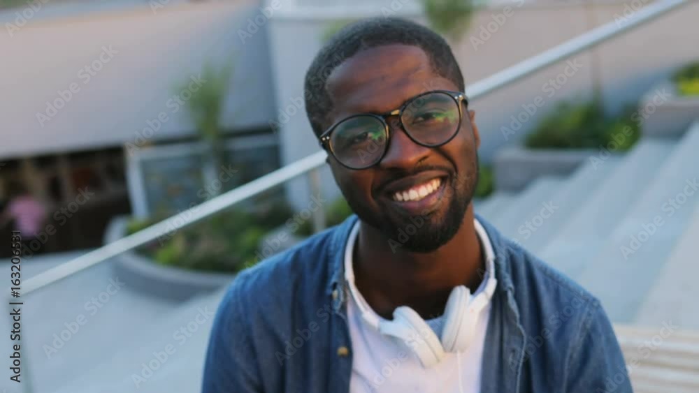 Portrait of handsome african man with glasses and headphones posing to the camera on background with stairs. Outdoor. Portrait of handsome african man with glasses and headphones posing to the camera on background with stairs. Outdoor.