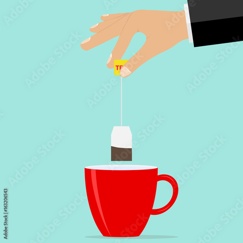 The hand holds a teabag over the cup. Brew tea