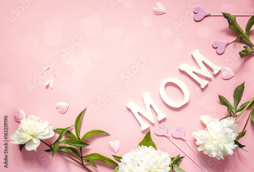 Mothers day background with white peonies and decorative hearts on pink table.