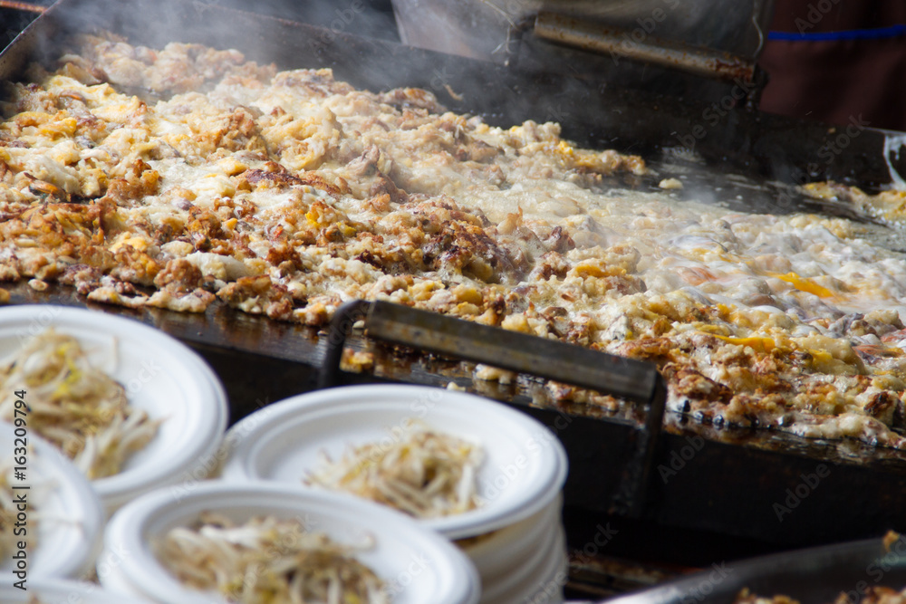 Cooking in thai food :Fried mussel pancakes or Oyster omelette (Hoi Tod) in local street food market. Traditional fried mussel stand in Thailand at street food vendor market Cooking in thai food :Fried mussel pancakes or Oyster omelette (Hoi Tod) in local street food market. Traditional fried mussel stand in Thailand at street food vendor market