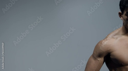 A male fitness model flexes his bicep and stretches out his arm. Filmed from close up and in isolation.