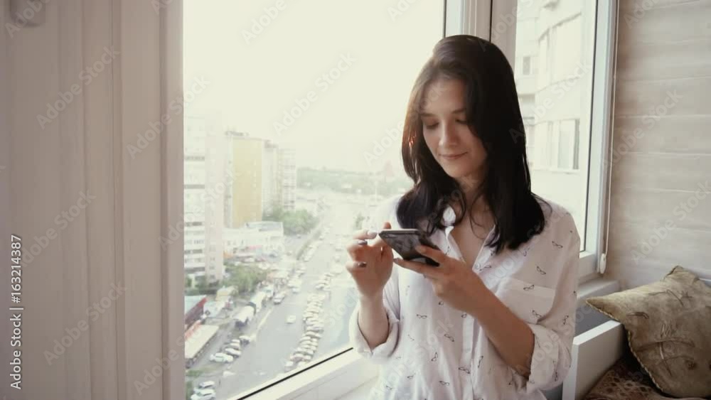 Woman using mobile smart phone in front of the big window. Slow motion 120 fps Woman using mobile smart phone in front of the big window. Slow motion 120 fps