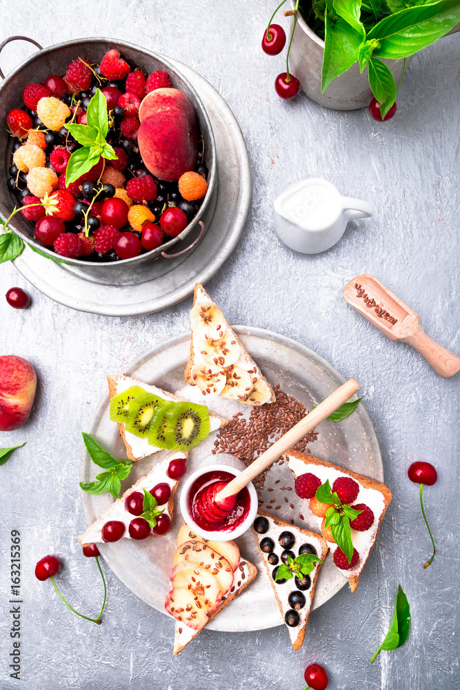 Fruit toast on grey background. Healthy breakfast. Clean eating. Dieting concept. Grain bread slices with cream cheese and various fruit, berries, seeds. Vegetarian. Top view.