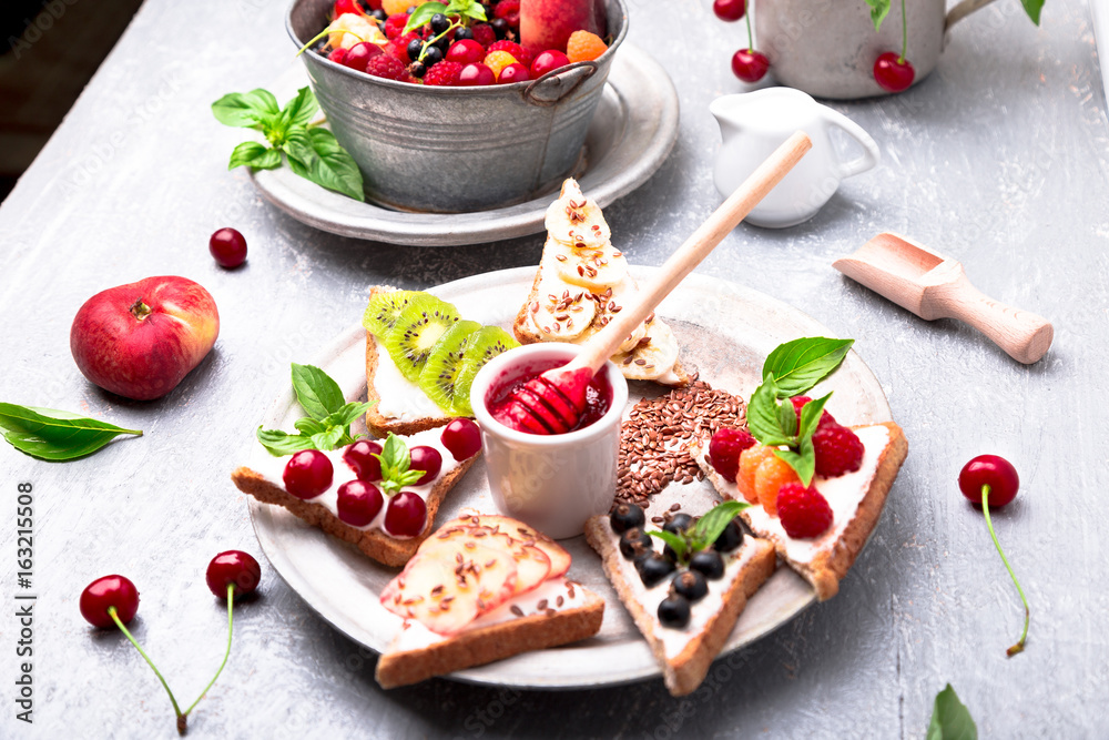 Fruit toast on grey background. Healthy breakfast. Clean eating. Dieting concept. Grain bread slices with cream cheese and various fruit, berries, seeds. Vegetarian.