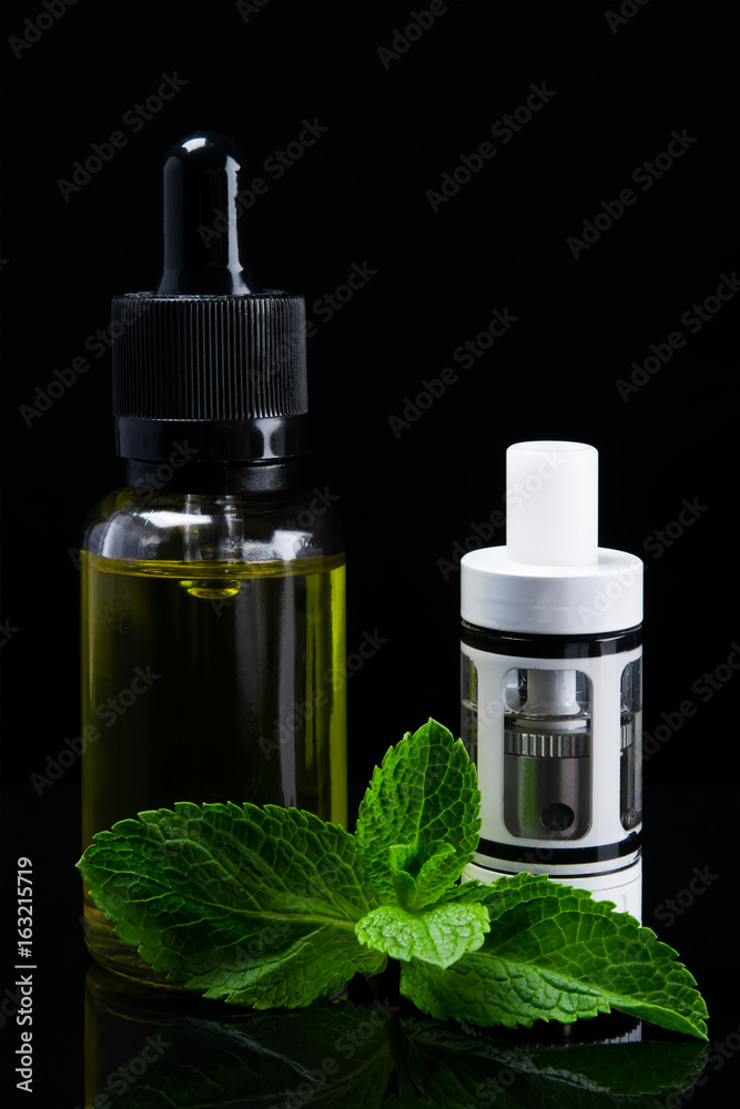 A white tank for an electronic cigarette stands next to a mint fluid A white tank for an electronic cigarette stands next to a mint fluid