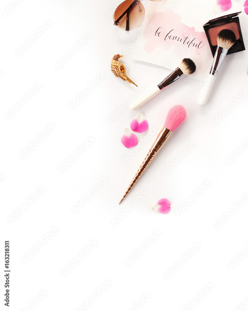 Top view of cosmetics and female accessories on white with pink petals and inspirational words written in calligraphy style `Be beautiful`. Beauty blog flat lay concept. Top view of cosmetics and female accessories on white with pink petals and inspirational words written in calligraphy style `Be beautiful`. Beauty blog flat lay concept.
