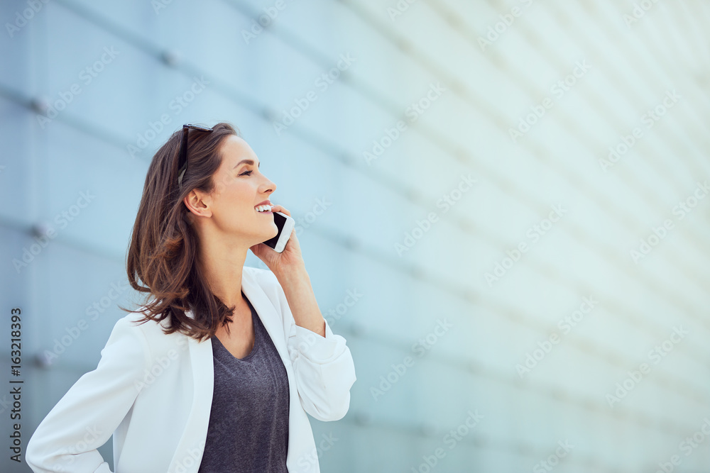 Fashionable and pretty girl laughing and talking on phone in outside setting Fashionable and pretty girl laughing and talking on phone in outside setting