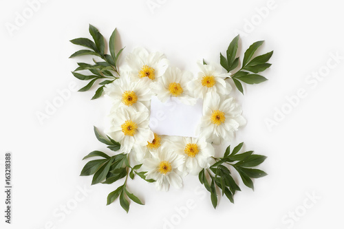 Mother s Day concept. Blank paper with heart-shaped floral frame made of white peony flowers and big green leaves. Top view  flat lay postcard.