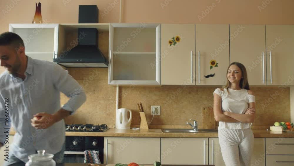 Attractive loving couple having fun in the kitchen. Handsome man juggle with apples to impress his girlfriend Attractive loving couple having fun in the kitchen. Handsome man juggle with apples to impress his girlfriend