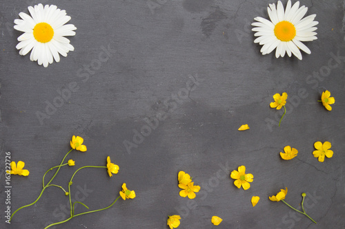 Yellow buttercups and white chamomiles on stone background. Floral frame. Top view.