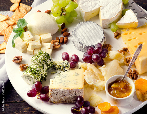 Cheese plates served with grapes, jam,  and nuts on a wooden board.